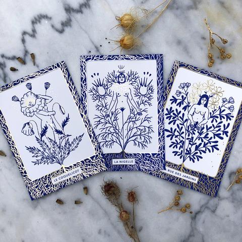 Trois cartes sont posées sur une table en marbre. Chacune des cartes représente une chimère-plante. De gauche à droite : le coquelicot, la nigelle et la rue des jardins.