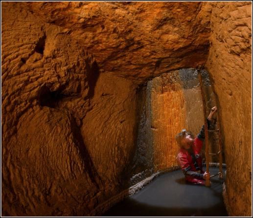 Un puits entre deux niveaux dans une carrière calcaire, le niveau le plus bas étant inondé.
Une personne sort de l'eau et grimpe les échelons permettant de rejoindre le niveau supérieur.