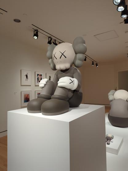 a sitting gray and white figure by kaws