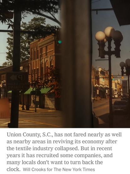 A quiet downtown street in Union County, South Carolina, featuring brick buildings, traffic lights, and lampposts. The scene reflects a historic area, with signs indicating public parking. A soft sunlight casts a warm glow, suggesting a late afternoon ambiance