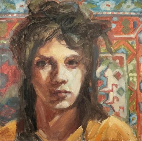A white woman with messy long hair, some of it up, in front of a colorful Kilim in soft reds, light blue, green & ivory. She is wearing a gold emergency blanket and looks directly at viewer.