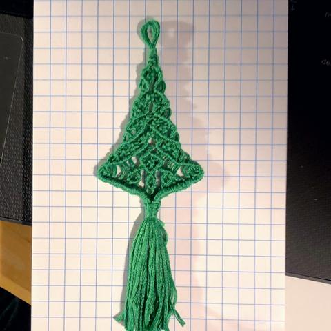 An intricate green macramé Christmas tree done in threads laid out on a small graph paper pad