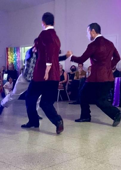 Their backs to the camera, the twins each hold one of Leonardo’s hands. His weight is on his bent left leg, and his right leg is kicked out far behind him.