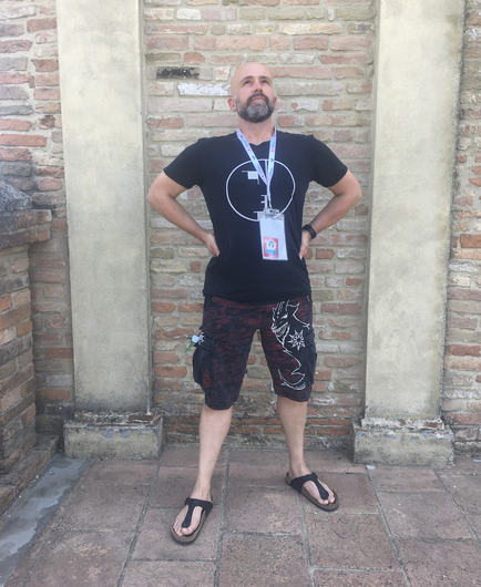 Heiko, standing tall, on the balcony of Bertinoro castle during ISWS 2022. He is wearing shorts and a black t-shirt.