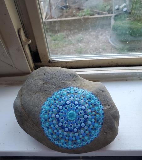 A brown rock sits on a white windowsill. A circle of dots in 5 colors of blue has been painted on to the right of the rock. Dots vary in size