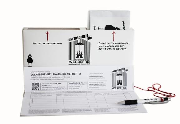 Eine gefaltete Papp-Box für Flyer und Unterschriftenlisten, die man oben einwerfen kann. Unten liegen Unterschriftenlisten und Informationen aus. Es hängt ein Stift daran.