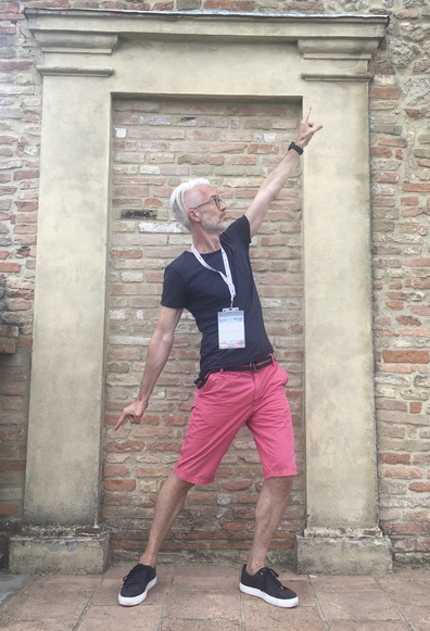 ISWS 2025 co-director and tutor Harald Sack (FIZ Karlsruhe - Leibniz Institute for Information Infrastructure & KIT Karlsruhe) standing tall in a "John Travolta" Staying Alive pose on the balcony of Bertinoro castle. He is wearing red shorts and a dark blue t-shirt.