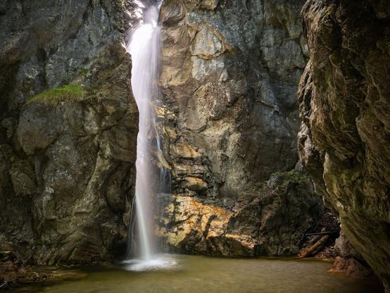 Das Bild zeigt einen Wasserfall, durch den sich das Wasser in einer großen Fallstufe nach unten bewegt. Die Szene ist in goldenes Licht getaucht.
