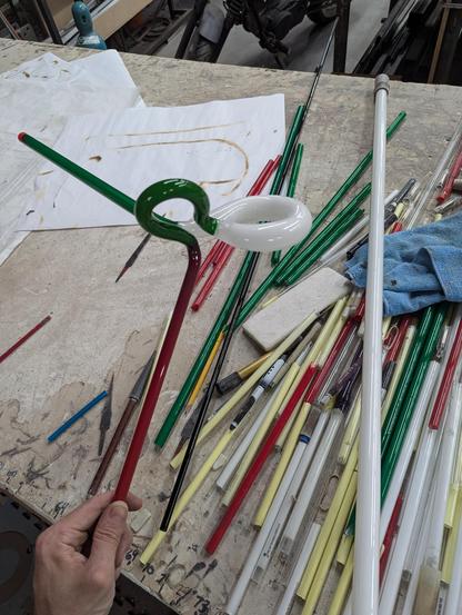 An emerald loop, with a big white loop, with a straight emerald tube and a straight ruby tube. Straight tubes in those colors (and others) scatter the table, along with a larger straight, 25mm diameter tube. On drywall.