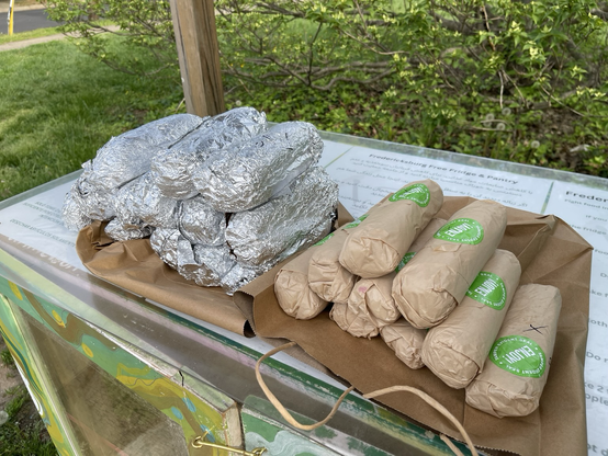 22 submarine sandwiches. Some in brown paper wraps, some in tin foil. A seal sticker says "Enjoy!".