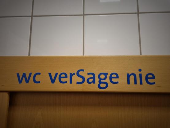 Blaue Folienbuchstaben auf einem Türrahmen: 

wc verSage nie