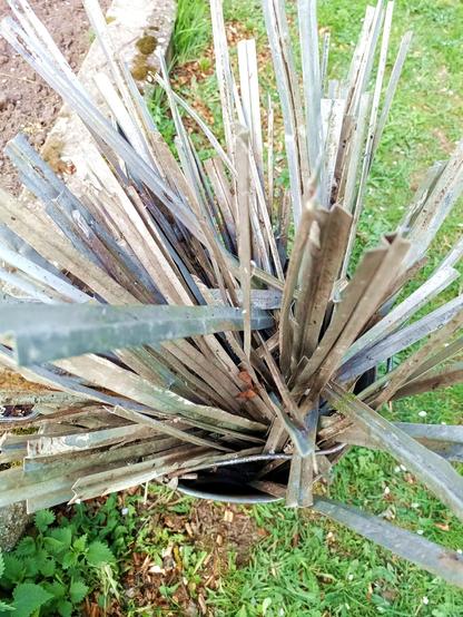 Close-up of a bucket of those aluminium profiles. They're folded in the shape of a ⚡. They look like they've been used before, there's some glue or sealant on most of them and they're bent and dented. They're also somewhat dirty from laying under a bush.
