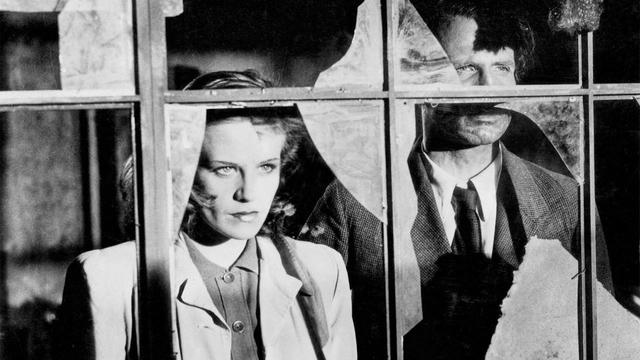 Film still: The faces of actors Hildegard Knef and Wilhelm Borchert looking outside through the broken glass of the apartment they share in the movie.