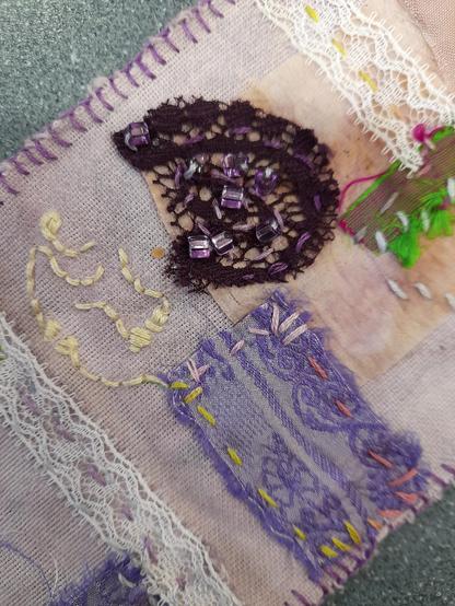 Detail showing pieces of lace (white and dark purple) and a piece of saree silk. The embroidery stitches in yellow, grey and rose are wild and intuitive.