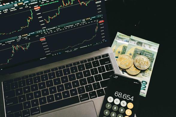 Symbolfoto für Kryptowährung: Ein Laptop mit Kursen, ein Taschenrechner auf dem Smartphone, Bargeld. Bildquelle: Pexels/Alesia Kozik