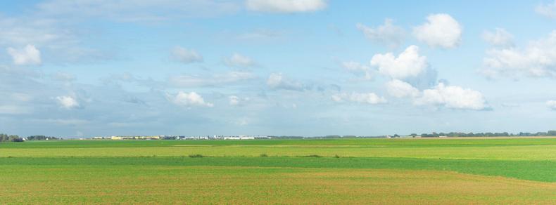 The image shows a vast, open landscape with green fields under a blue sky with scattered clouds. It's a serene rural scene, possibly of farmland or pasture.