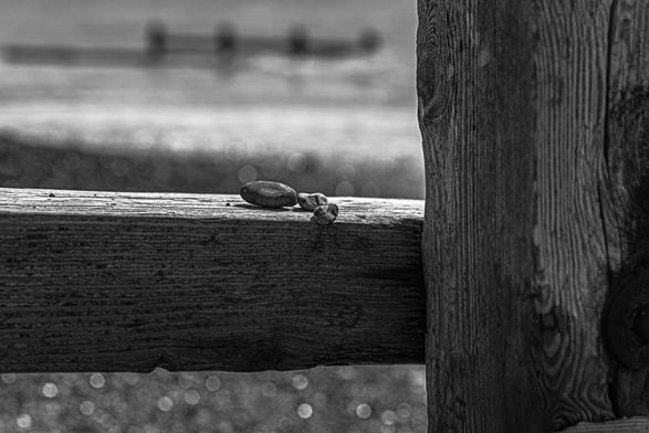 Pebbles on a groyne on Goring beach. A black and white photograph, a shallow depth of field forces focus on the pebbles, the light catching the shingle beach forming bokeh in the distance.