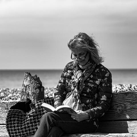 A lady reads, seated on a groyne on Goring beach. She is alone, the book her only companion. The black and white photograph frames her against the sky, windswept hair and glasses contrasting with the sky that falls in tone around her.