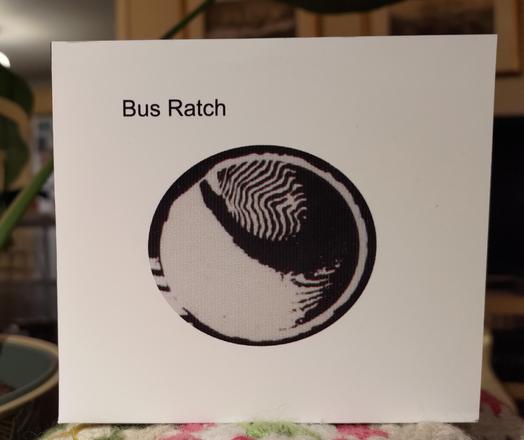 White folded-paper CD cover. "Bus Ratch" in upper left side. 

A circle with some black and white abstract artwork in the middle.