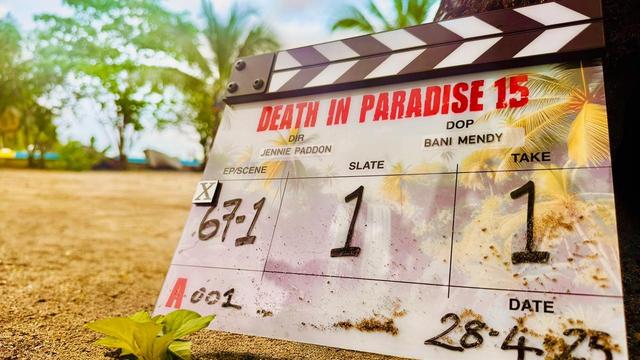 Clapperboard for Death in Paradise Season 15, Episode 67/Scene 1, Slate 1, Take 1, Date: 250428. In the background strand, palm trees, ocean and blue sky.