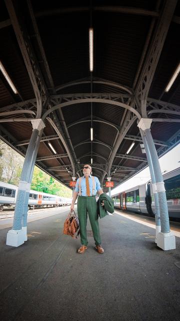 Me, a middle aged bald white guy with a beard. Wearing a nice green tweed suit, gold knit tie and glasses. Standing on a station platform.