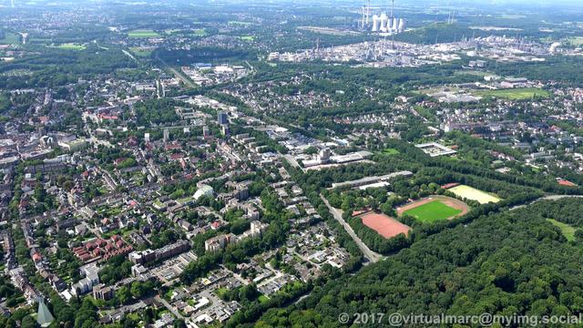 An aerial photo of Gelsenkirchen Buer. You can see some active industry in the background. There are many trees near the living and working quaters.