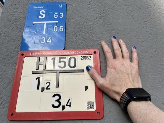 Hand mit bunten Fingernägeln auf einem Hydrantenschild
