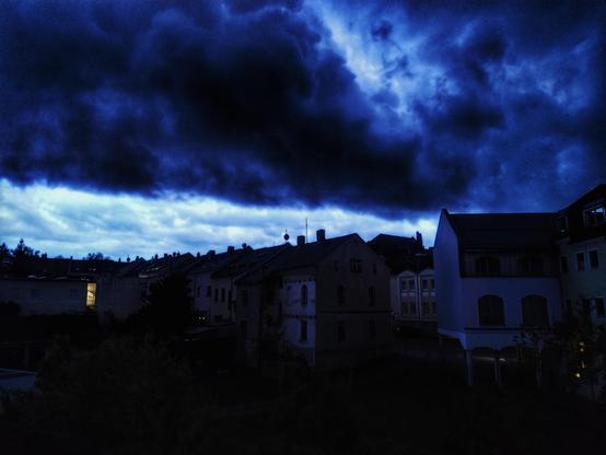 Dunkle Wolken über den Häusern, am Horizont noch ein Lichtstreifen am Himmel.