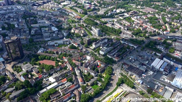 An aerial photo of the center of Essen with living and working quaters sourrounded by trees. A big Y-Shaped black building can be seen on the left, this is the city hall of Essen.