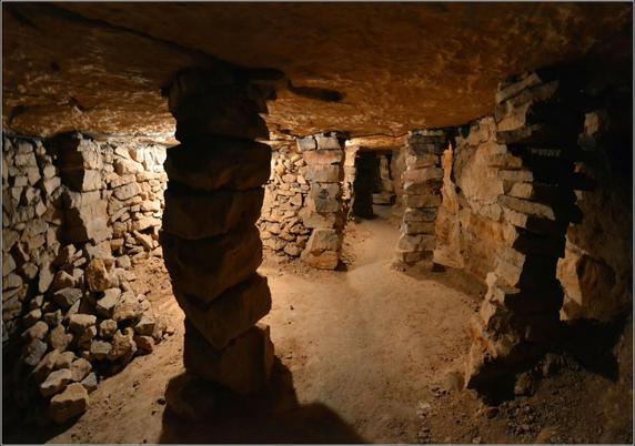 Une galerie dans une carrière souterraine. Des piliers constitués de blocs de calcaire soutiennent le ciel.
Des murs en pierres sèches retiennent les remblais.