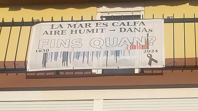 Lona en balcón bañado en sol. Pocas palabras, para que se lea desde abajo:

La mar es calfa.
Aire humit (flecha) DANAs
FINS QUAN?

De fondo, el gráfico de barras de colores mostrando el aumento de la temperatura anual promedio de la ciudad de Valencia entre 1850 y 2024. Este último año está marcado con un lazo negro, por la catástrofe de la DANA, más trágica por la criminal irresponsabilidad de quienes nos gobiernan.