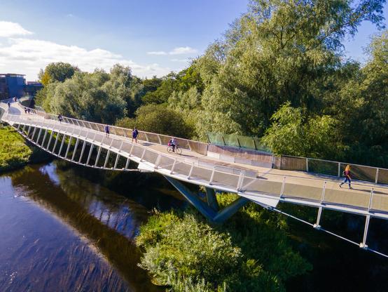 Photograph of a pedestrian bridge spanning a wide river lined with dense, mature trees