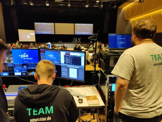 Foto in den Raum. Vorne das Techteam mit FeedBeat auf den Bildschirmen. Auf der Bühne FeedBeat Zuschauerapp und Publikumsraum.