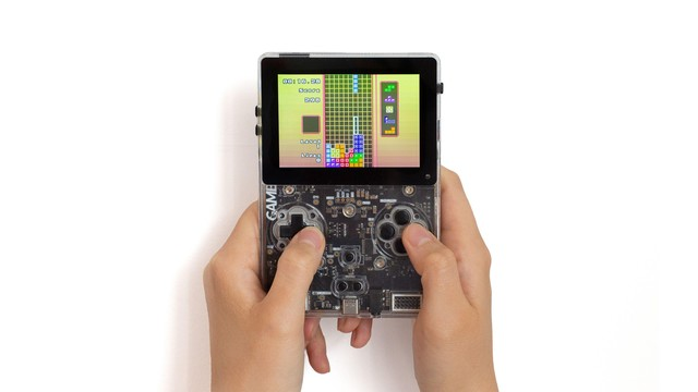 Someone playing tetris on a "game-bub" handheld. It's the same form factor as a gameboy color but it's a clear plastic shell so you can see the black PCB inside and the screen is a larger IPS LCD.