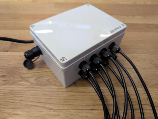 A grey electronics box with 8 wires coming out one side, a waterproof Ethernet port on another, and a power cable coming out the back.