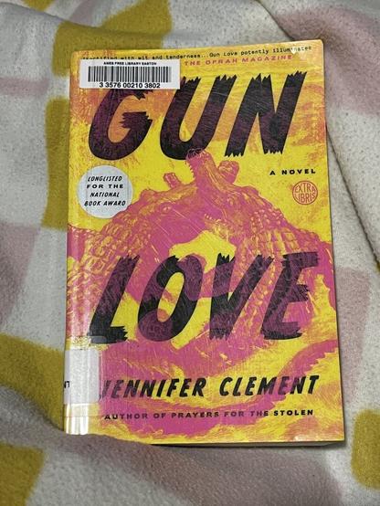 the cover of a yellow softcover book, featuring two conjoined pink crocodiles, biting each other’s snouts. the book is titled GUN LOVE, and is by jennifer clement.