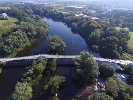 Aerial photo of a pedestrian bridge spanning a river lined with dense, mature trees