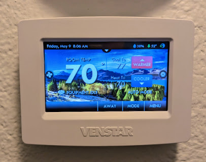 A Venstar smart thermostat mounted on a wall displays a temperature of 70°F on its color touchscreen. The interface shows the current date (Friday, May 9) and time (8:06 AM), along with status indicators for battery and WiFi connection, and features control buttons for mode selection across the bottom of the screen.

(Description assisted by Claude AI.)