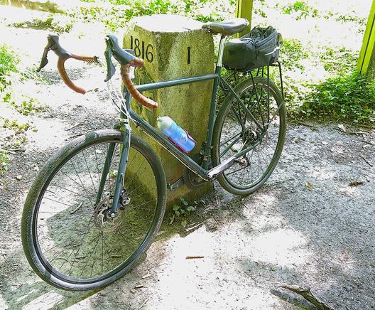 Photo of my bicycle propped up against a boundary stone on the Swiss-French border. One face of the stone pillar has the number 1 engraved in it. The other face has the date 1816 and an image of an eagle and a key.