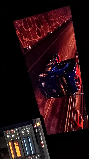 The photograph composed in total darkness shows a computer screen displaying a video game scene. The scene is set at night on a road with a stone wall on the left side. A blue truck is on the road, with a red car visible in the background. The road is illuminated by red and orange lights, creating a dramatic atmosphere. The screen also shows a software interface with various metrics, including CPU temperature at 57°C, GPU load at 100, and other performance indicators. The interface includes sliders and buttons, suggesting it is a monitoring tool for the computer's hardware. The overall color scheme is dark with red and orange highlights, emphasizing the nighttime setting and the game's action.

 Ovis2-8B

🌱 Energy used: 0.180 Wh