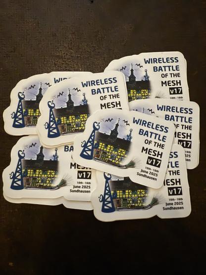 A collection of stickers for the "Wireless Battle of the Mesh v17" event, featuring images of radio towers and a building, with dates listed as June 10th to 16th, 2025, in Sundhausen.