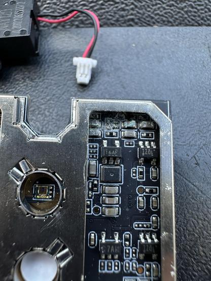 Close-up of a circuit board featuring various electronic components, including resistors and capacitors. A connector and wiring are visible, indicating connections for power or data. The surface appears slightly worn or dirty.