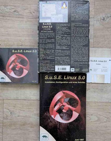Das Bild zeigt die Verpackung, das Handbuch, eine CD Hülle für 4 CDs und eine weiße 3,5 Zoll Bootdiskette von SuSE Linux 5.0 aus dem Jahr 1997.