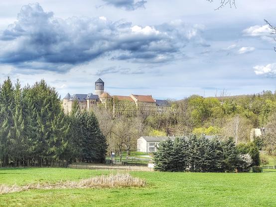 Schloss Voigtsberg umrahmt vom Grün der Frühlingslandschaft. Der blaue Himmel etwas bewölkt.