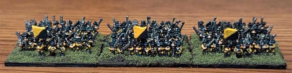 Photo of six bases of 3 mm Doppelsöldner miniatures from Microworld Games. Each base has three ranks of troops dressed in yellow with black hats and boots carrying Zweihänder swords. The front ranks of three bases have command models, including a drummer and standard bearer, the standard painted yellow and black per bend sinister.