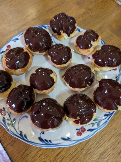 A plate of cream puffs, some showing bits of pastry cream. All coated with chocolate ganache.