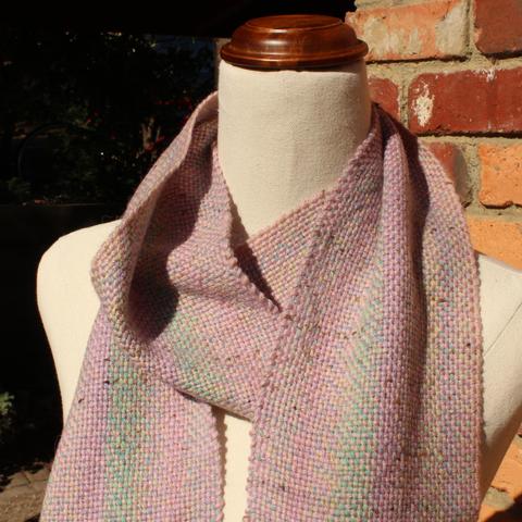 Neck and shoulders of a dress form. There is a scarf wrapped around the neck. The scarf is broadly pink, but has soft stripes of blue, purple, green and yellow running lengthwise.