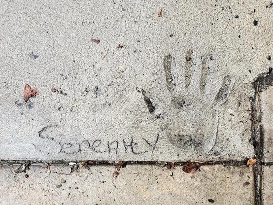 Photo of a hand print in a cement sidewalk. The word "serenity" is inscribed to the left of the hand print.
