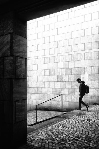 Black and white. Portrait format. Silhouette of a passer-by walking down a short flight of stairs.