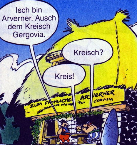 Asterix und Obelix sitzen an einem Tisch vor einer Taverne. Der Name der Taverne ist "Zum fröhlichen Arverner".